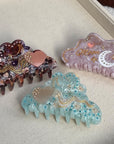 A trio of 10cm celestial-themed acetate hair clips in pink with a moon motif, burgundy with a heart, and marbled teal with rhinestone accent