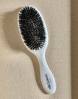 White hairbrush with black mixed boar and nylon bristles on a beige fabric background - Slik & Sleek London salon quality brush