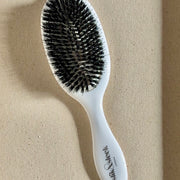 White hairbrush with black mixed boar and nylon bristles on a beige fabric background - Slik & Sleek London salon quality brush