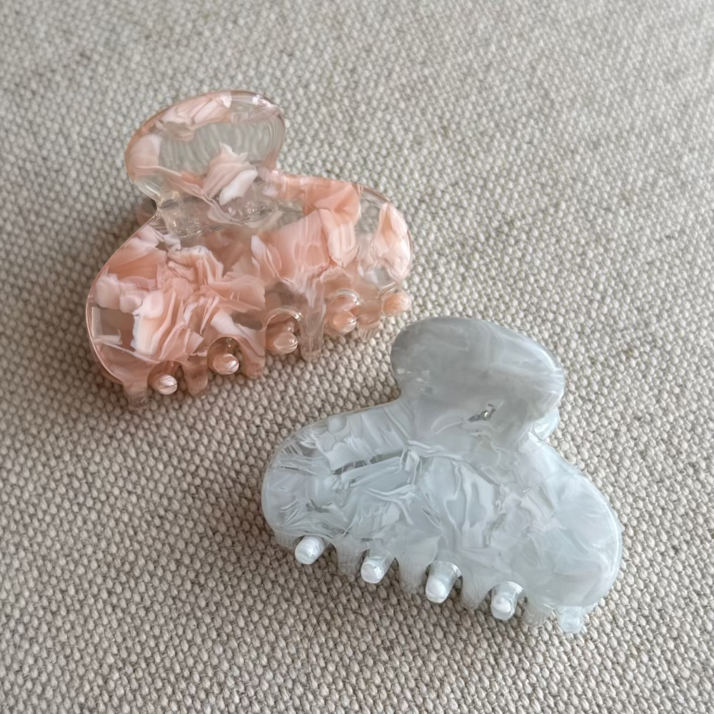 Two hair clips, one pink and one gray, on a textured beige surface.