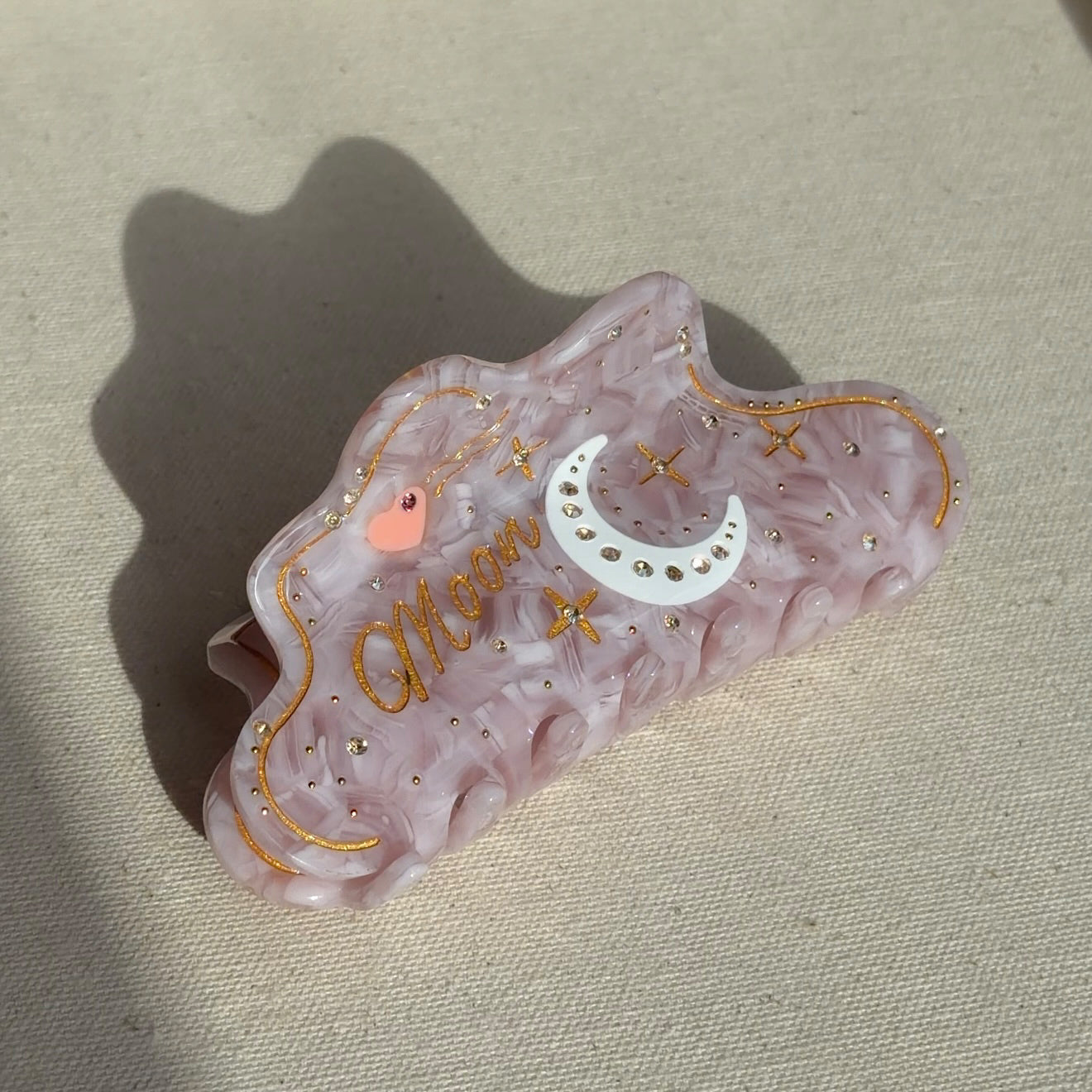 A 10cm celestial-themed acetate hair clip in pink with a moon motif with rhinestone accent