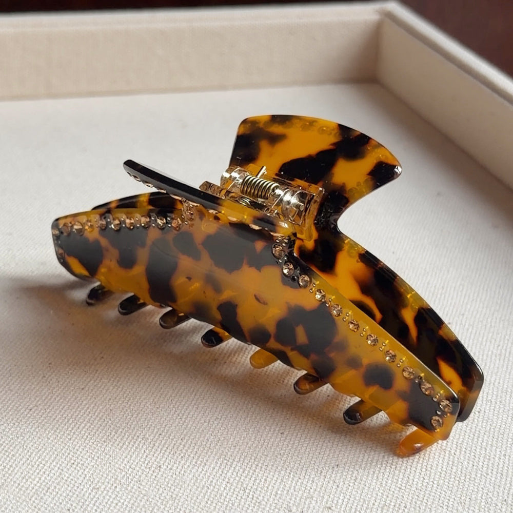 Tortoiseshell patterned hair clip with rhinestones on a light fabric background