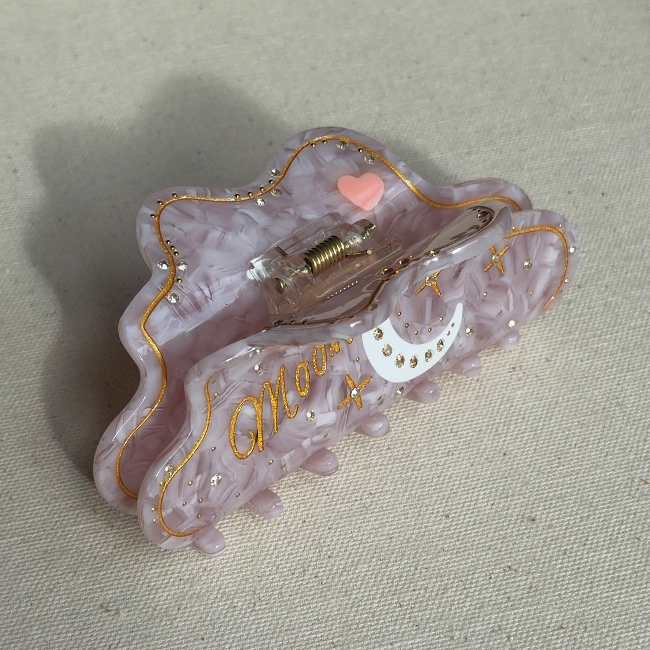 A 10cm celestial-themed acetate hair clip in pink with a moon motif with rhinestone accent